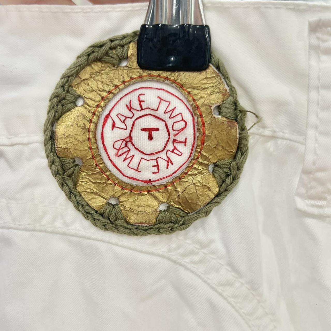 Handcrafted circular patch with gold, green, and red embroidery on white sustainable fabric
