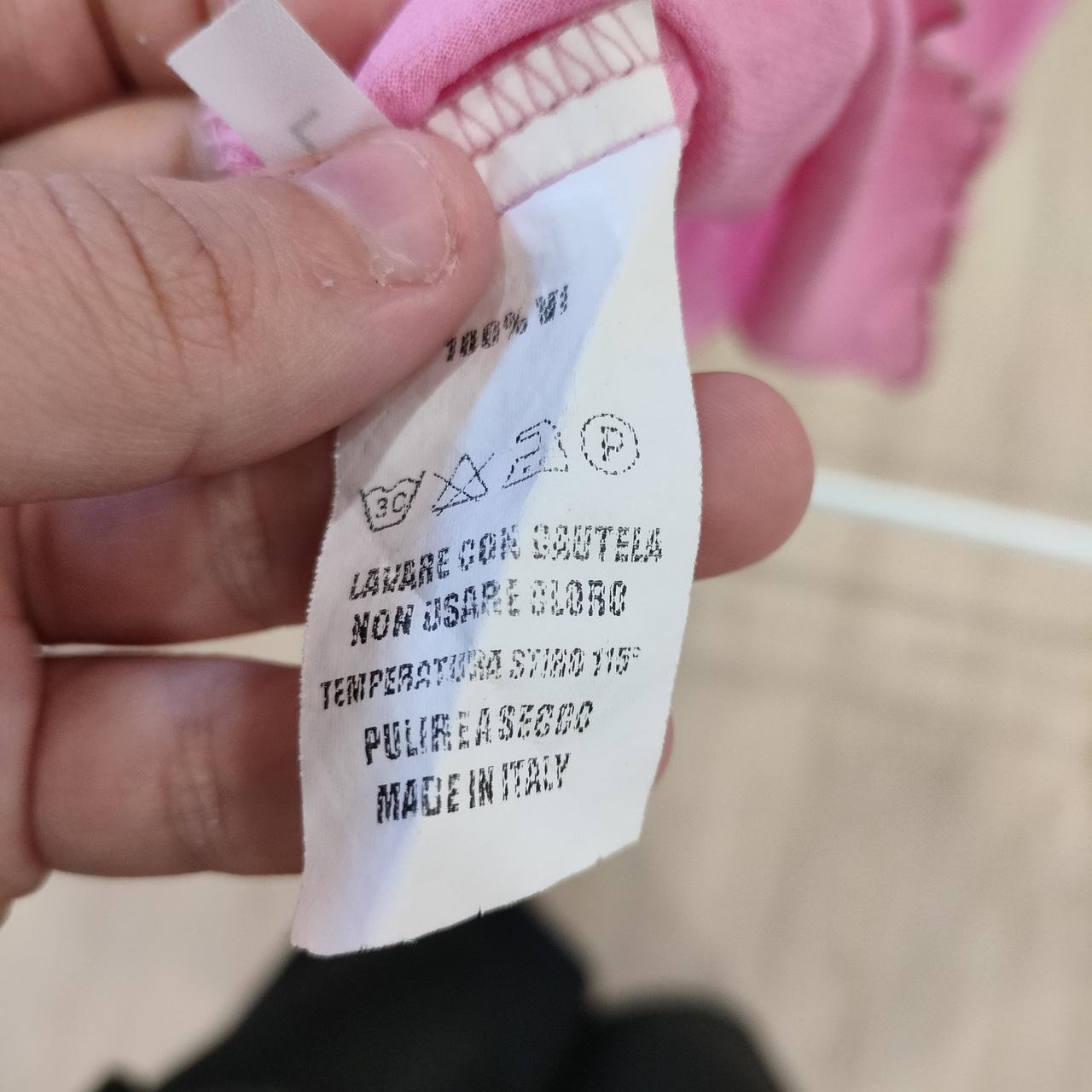 Hand holding pink sustainable fashion garment with visible Italian care label
