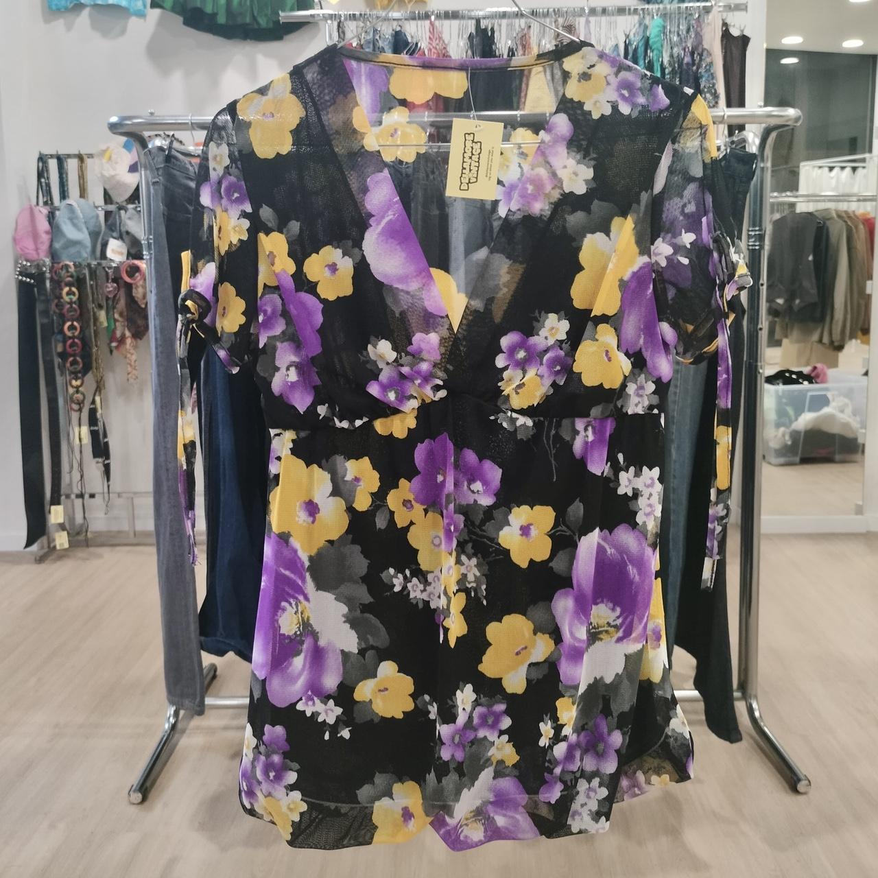 Sheer black floral blouse with yellow and purple flowers hanging in a second hand fashion store