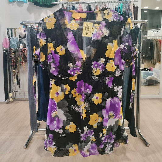 Sheer black floral blouse with yellow and purple flowers hanging in a second hand fashion store