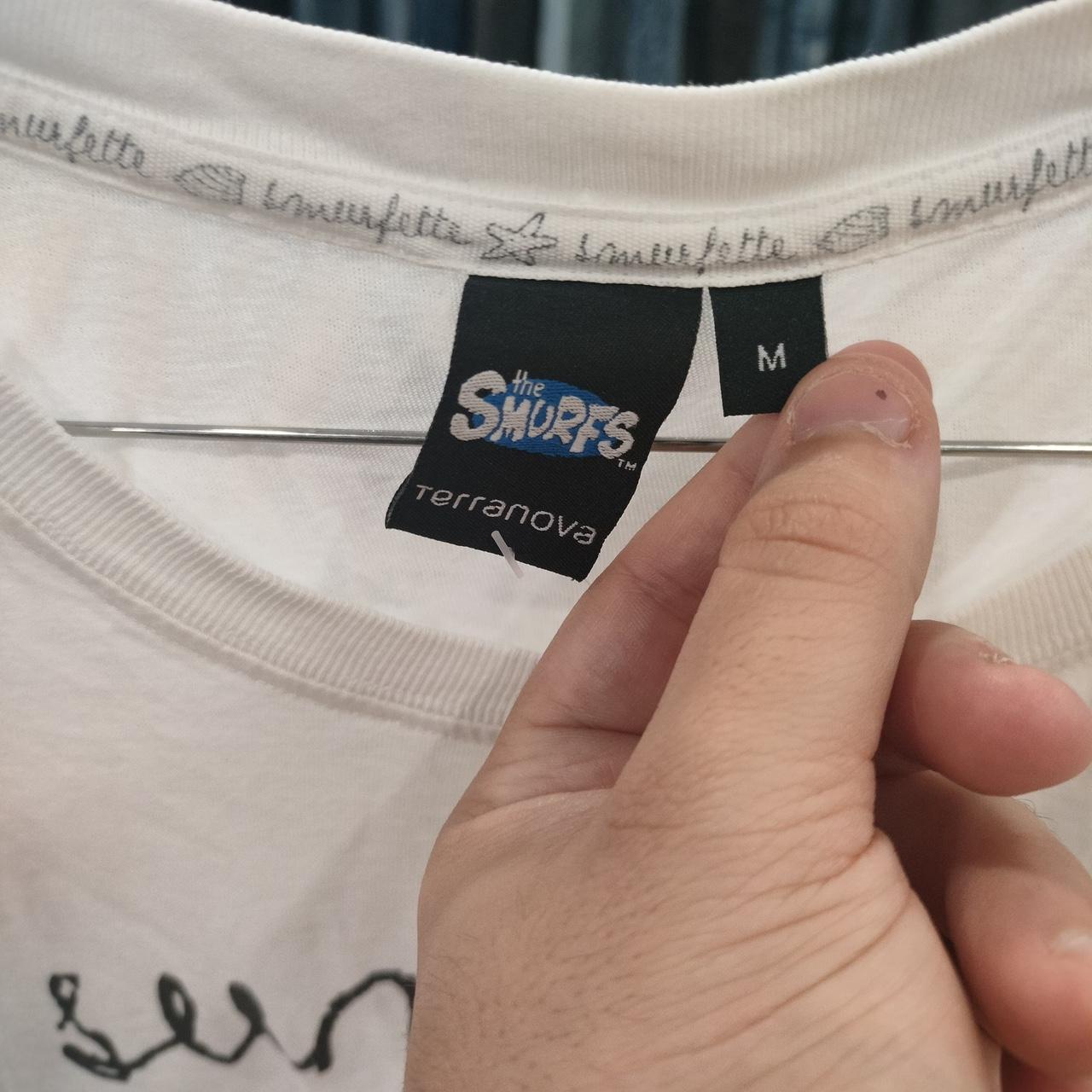 Hand holding a white The Smurfs Terranova t-shirt, size medium, close-up of labels