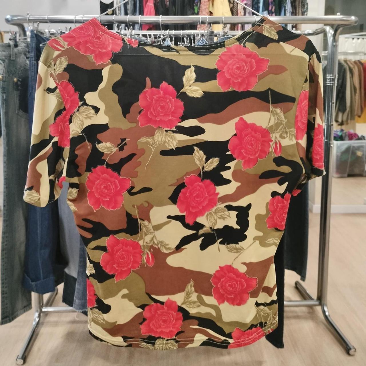 Short sleeve shirt with camouflage and red rose floral print, hanging in a clothing store