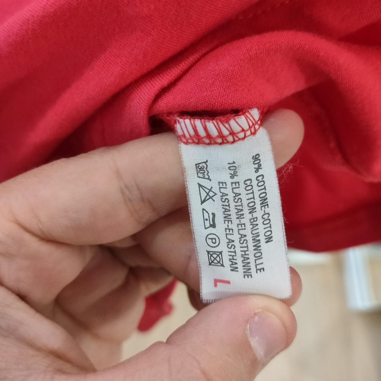 Clothing label held by a hand against a red fabric background