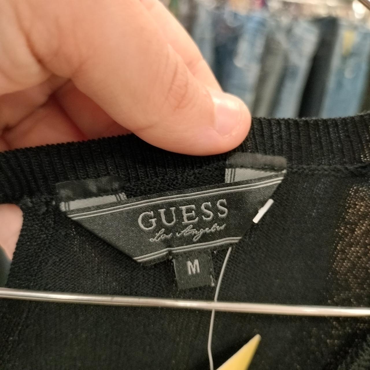 Close-up of a Guess label on black fabric with a hand holding it