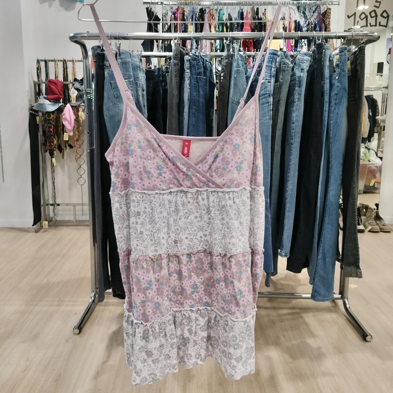 Pink and white floral tiered spaghetti strap dress displayed in front of denim jeans rack