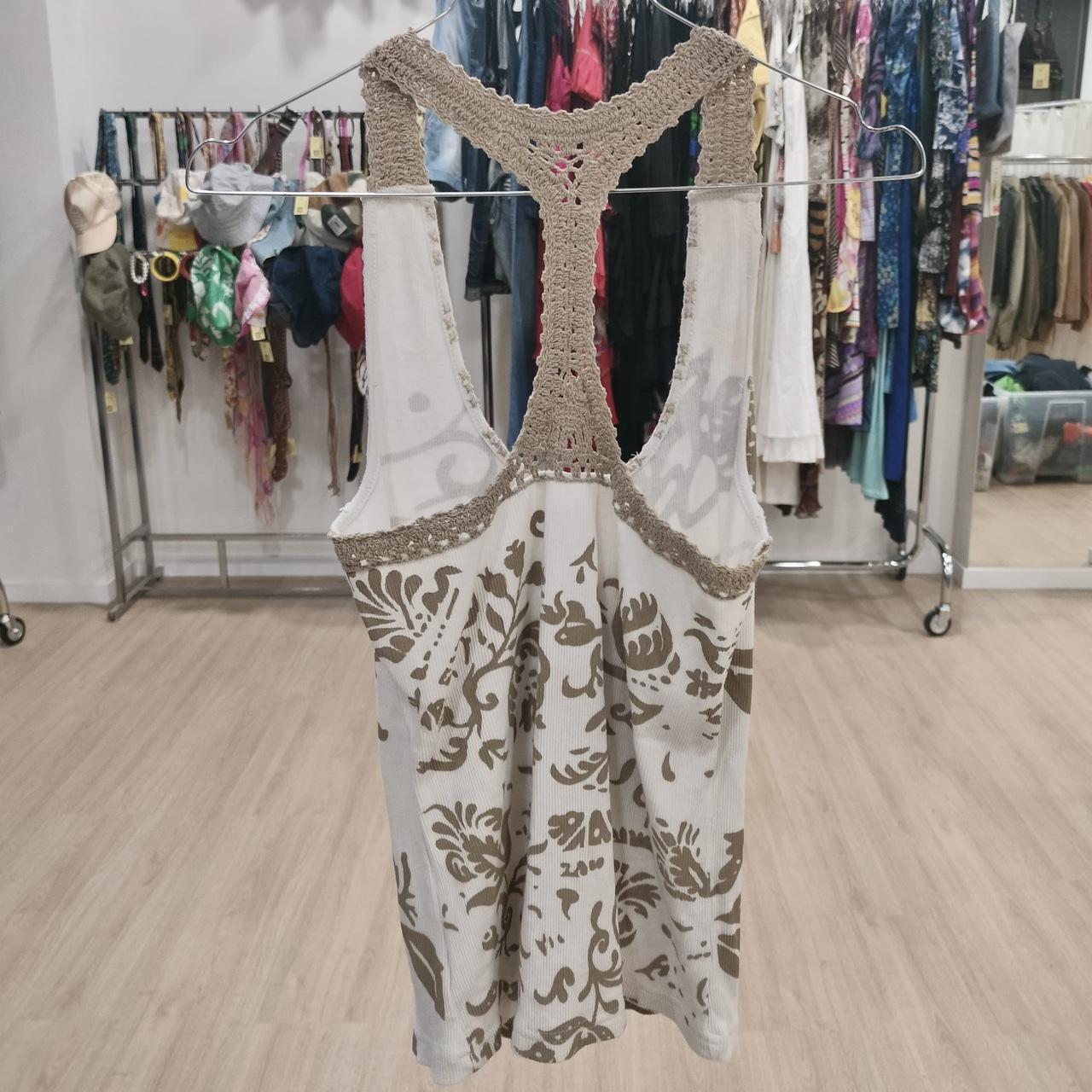 Beige and white crochet racerback tank top with floral pattern, hanging in a second hand fashion store