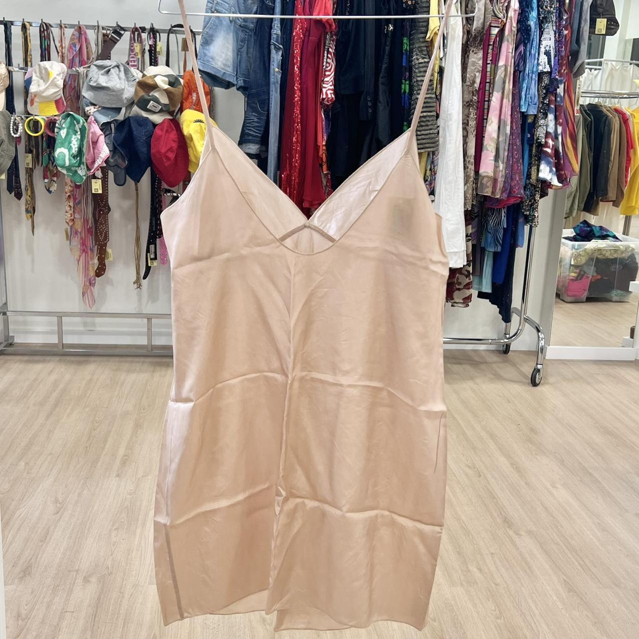 Beige slip dress hanging in a clothing store with racks of clothes in the background