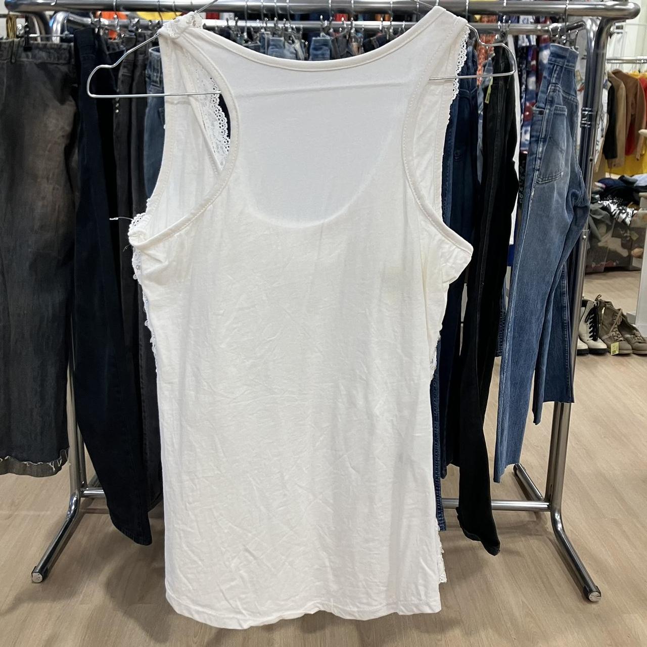 White sleeveless tank top with lace trim on a rack among second hand jeans