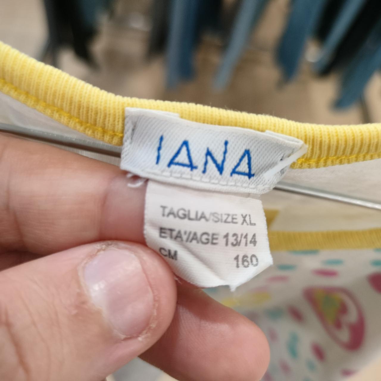 Hand holding clothing tag showing IANA XL size, yellow collar, age 13-14, 160 cm height