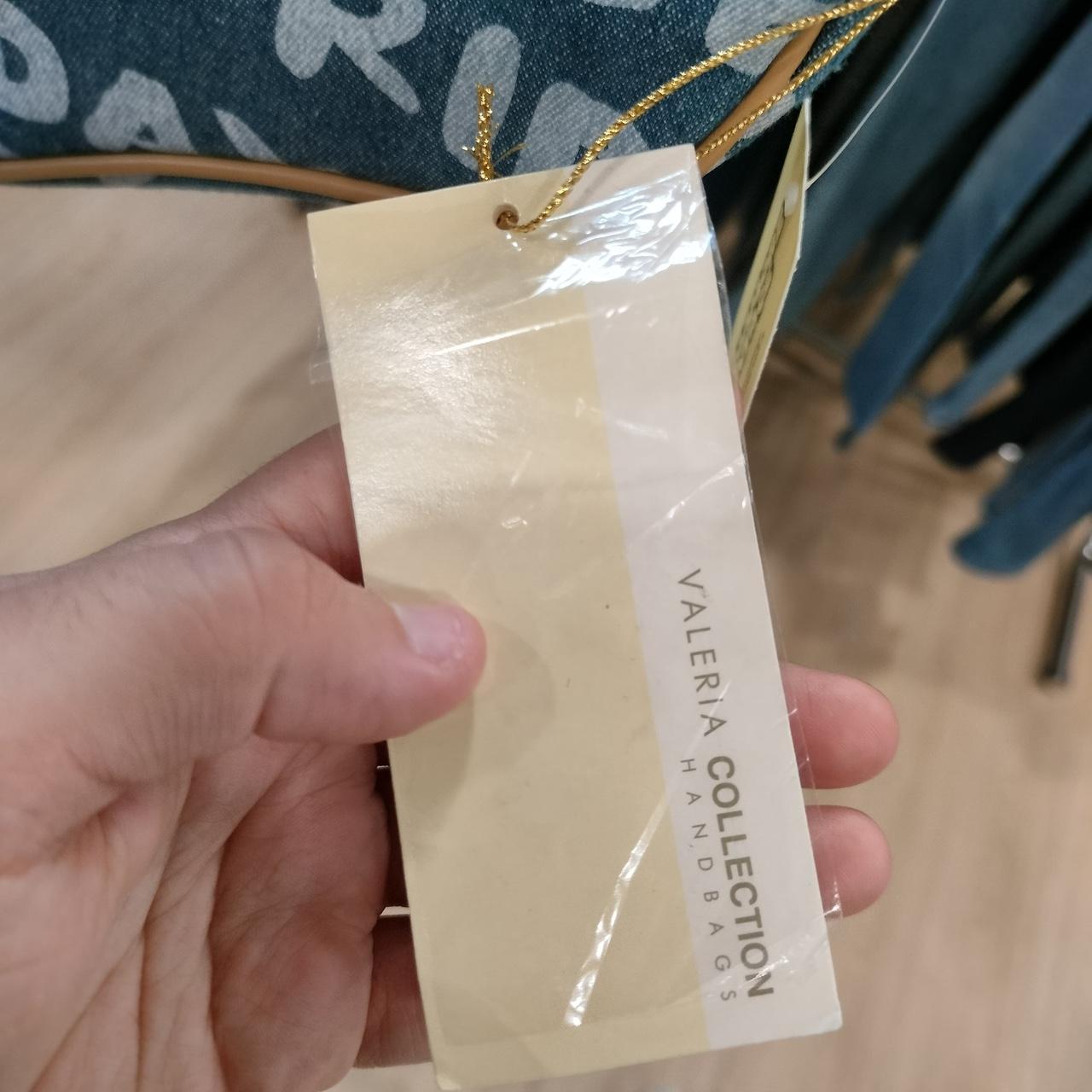 Hand holding a Valeria Collection handbag tag with a blurred background